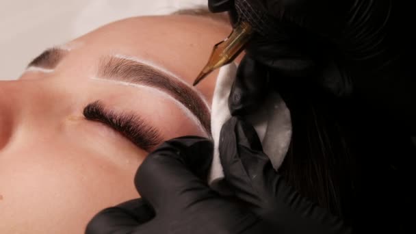 Øjenbryn permanent make-up. Føreren i studiet introducerer sort pigment under huden på en ung model ved hjælp af en speciel maskine. Moderne tatovering til skønhed – Stock-video