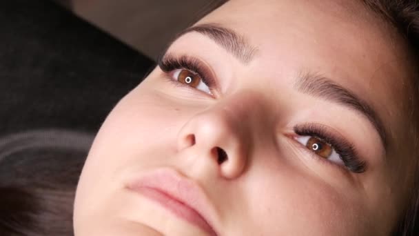 Le beau visage d'une jeune fille modèle qui se trouve sur un canapé dans un salon de beauté avant d'appliquer microblading, tatouage permanent de sourcil de maquillage et lèvres poudrées — Video