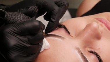 Kaş kalıcı makyaj malzemesi. Stüdyodaki usta, özel bir makine kullanarak genç bir modelin derisinin altında siyah pigmenti tanıtıyor. Güzellik için modern dövme yakın görünüm