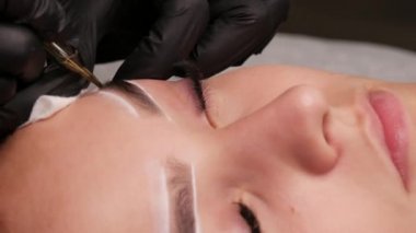 Kaş kalıcı makyaj malzemesi. Stüdyodaki usta, özel bir makine kullanarak genç bir modelin derisinin altında siyah pigmenti tanıtıyor. Güzellik için modern dövme yakın görünüm