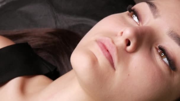 Le beau visage d'une jeune fille modèle qui se trouve sur un canapé dans un salon de beauté avant d'appliquer microblading, tatouage permanent de sourcil de maquillage et lèvres poudrées — Video