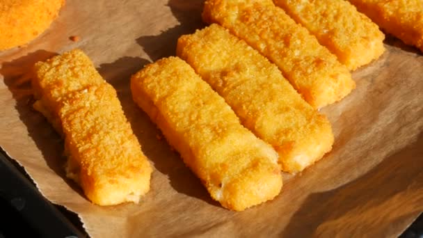 Queso Camembert en masa en un porche con una bandeja para hornear al lado de los palitos de pescado en la masa. Preparación de comida rápida — Vídeos de Stock