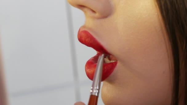 Maquillaje labial brillante, grandes labios hermosos están pintados con lápiz labial rojo con un cepillo especial en un salón de belleza. Maquillaje profesional vista de cerca — Vídeo de stock