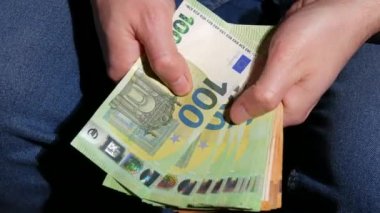 Erkek eller odadaki deri koltukta otururken euro banknotlarını sayıyorlar. Para dizlerinin üstüne çöker. Para, ödeme, tasarruf, bankacılık konsepti, tatil, araba, kazançlar için tasarruf