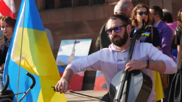 Estrasburgo, Francia - 26 de marzo de 2022: Manifestación en apoyo de Ucrania contra la guerra con Rusia. Un músico toca instrumento musical contra banderas ucranianas y carteles para detener la guerra. — Vídeo de stock