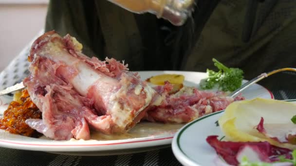 Mãos masculinas cortam uma junta de porco com um garfo e uma faca em um restaurante na rua — Vídeo de Stock