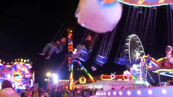 April 24, 2022 - Kehl, Germany: Amusement park at night. Visitors ride on various entertainment attractions. Bright multi-colored lights and lamps glow in the evening — Video