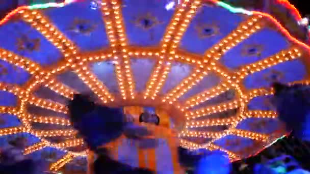 Carrusel nocturno en el que viajan los visitantes. Parque de atracciones por la noche en luces de colores. Iluminado alegre ir carrusel redondo — Vídeos de Stock