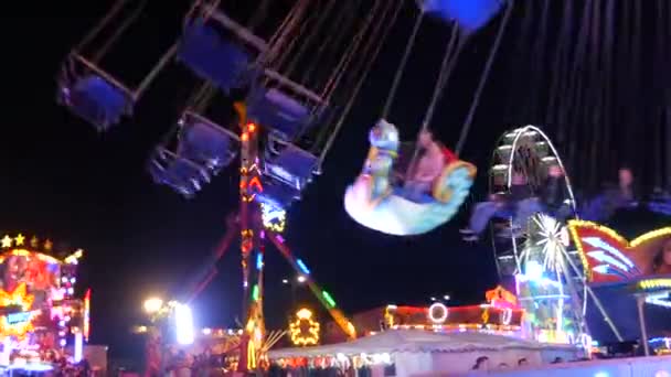 April 24, 2022 - Kehl, Germany: Amusement park at night. Visitors ride on various entertainment attractions. Bright multi-colored lights and lamps glow in the evening — Stock Video
