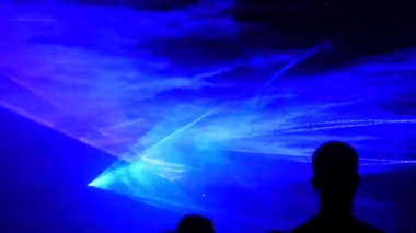 Açık hava performansı, gece gökyüzünün siyah arka planında hafif lazer gösterisine bakan bir sürü insan. Çok renkli lazer ışınları çeşitli şekillere dönüşür, dumandaki yansıma. Teknoloji Konferansı.