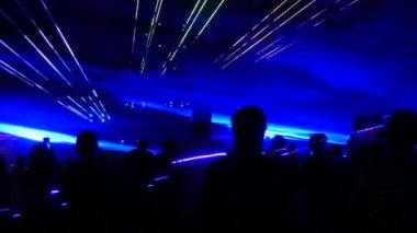 A modern laser light show, with a projection on smoke, a crowd of people watches the laser beams that turn into various lines and shapes. Outdoor performance