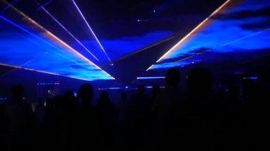 A modern laser light show, with a projection on smoke, a crowd of people watches the laser beams that turn into various lines and shapes. Outdoor performance