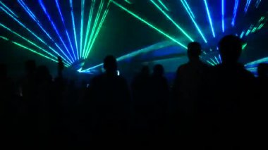 Modern bir lazer ışığı gösterisi, dumanla yansıtılan bir projeksiyonla, bir grup insan çeşitli çizgilere ve şekillere dönüşen lazer ışınlarını izliyor. Açık hava performansı