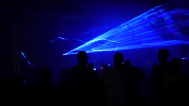 Crowd of people looking at light laser show on a black background of the night sky, outdoor performance. Multi-colored laser beams turn into various shapes, projection on smoke. Technology Conference.