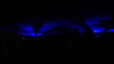 Modern bir lazer ışığı gösterisi, dumanla yansıtılan bir projeksiyonla, bir grup insan çeşitli çizgilere ve şekillere dönüşen lazer ışınlarını izliyor. Açık hava performansı