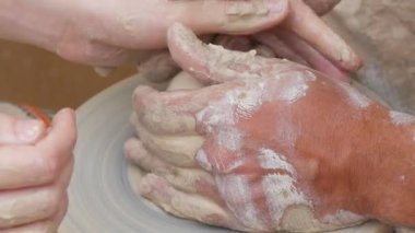 Kil modelliği ana sınıfı. Öğretmen çocuklara kilden tencere gösteriyor. Potter erkeği elleri, yaratıcı atölyede çömlekçi çarkında dönen yumuşak beyaz kil tenceresini şekillendirir ve şekillendirir. Çanak çömlek şekli.