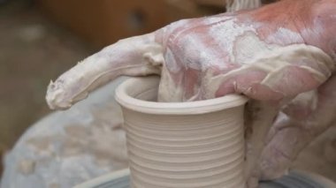 Kil modelliği ana sınıfı. Potter erkeği elleri, yaratıcı atölyede çömlekçi çarkında dönen yumuşak beyaz kil tenceresini şekillendirir ve şekillendirir. Çanak çömlek şekli.