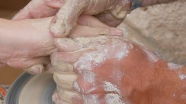 Kil modelliği ana sınıfı. Öğretmen çocuklara kilden tencere gösteriyor. Potter erkeği elleri, yaratıcı atölyede çömlekçi çarkında dönen yumuşak beyaz kil tenceresini şekillendirir ve şekillendirir. Çanak çömlek şekli.