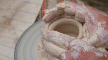 Kil modelliği ana sınıfı. Potter erkeği elleri, yaratıcı atölyede çömlekçi çarkında dönen yumuşak beyaz kil tenceresini şekillendirir ve şekillendirir. Çanak çömlek şekli.