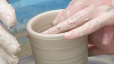 Kil modelliği ana sınıfı. Öğretmen çocuklara kilden tencere gösteriyor. Potter erkeği elleri, yaratıcı atölyede çömlekçi çarkında dönen yumuşak beyaz kil tenceresini şekillendirir ve şekillendirir. Çanak çömlek şekli.