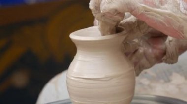 Kil modelliği ana sınıfı. Potter erkeği elleri, yaratıcı atölyede çömlekçi çarkında dönen yumuşak beyaz kil tenceresini şekillendirir ve şekillendirir. Çanak çömlek şekli.