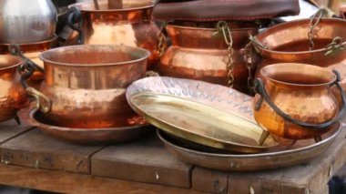 A large number of new and varied copper utensils on the counter of a stall in a street market. Bowls, bowls, pots and pans.