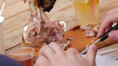 Bir adam et kesmek için özel bir çatal ve bıçakla kemiğin üzerinde büyük bir parça kızarmış et yiyor..
