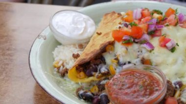 Mexican national dish tacos. Plate with tacos next to sauces, rice, legumes and cheese on the table of a summer cafe, close up view.