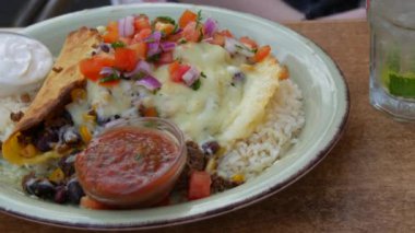 Mexican national dish tacos. Plate with tacos next to sauces, rice, legumes and cheese on the table of a summer cafe, close up view.