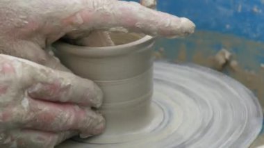 Kil modelliği ana sınıfı. Öğretmen çocuklara kilden tencere gösteriyor. Potter erkeği elleri, yaratıcı atölyede çömlekçi çarkında dönen yumuşak beyaz kil tenceresini şekillendirir ve şekillendirir. Çanak çömlek şekli.