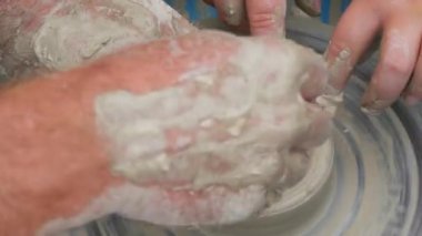 Kil modelliği ana sınıfı. Öğretmen çocuklara kilden tencere gösteriyor. Potter erkeği elleri, yaratıcı atölyede çömlekçi çarkında dönen yumuşak beyaz kil tenceresini şekillendirir ve şekillendirir. Çanak çömlek şekli.