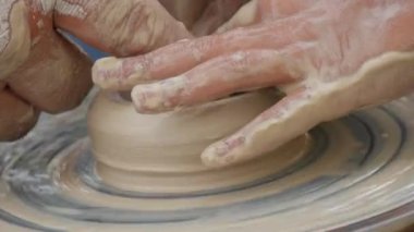 Kil modelliği ana sınıfı. Öğretmen çocuklara kilden tencere gösteriyor. Potter erkeği elleri, yaratıcı atölyede çömlekçi çarkında dönen yumuşak beyaz kil tenceresini şekillendirir ve şekillendirir. Çanak çömlek şekli.