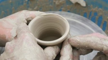 Kil modelliği ana sınıfı. Öğretmen çocuklara kilden tencere gösteriyor. Potter erkeği elleri, yaratıcı atölyede çömlekçi çarkında dönen yumuşak beyaz kil tenceresini şekillendirir ve şekillendirir. Çanak çömlek şekli.