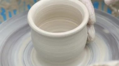 Kil modelliği ana sınıfı. Potter erkeği elleri, yaratıcı atölyede çömlekçi çarkında dönen yumuşak beyaz kil tenceresini şekillendirir ve şekillendirir. Çanak çömlek şekli.