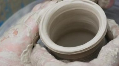 Kil modelliği ana sınıfı. Potter erkeği elleri, yaratıcı atölyede çömlekçi çarkında dönen yumuşak beyaz kil tenceresini şekillendirir ve şekillendirir. Çanak çömlek şekli.