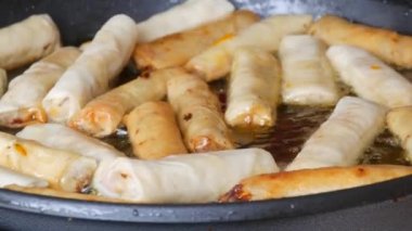 Asian spring rolls are fried in oil in a pan and turned over with kitchen tongs.