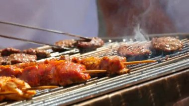 Grilled meat, burger patties and chicken fillet on skewers in smoke that turn the chef hand.