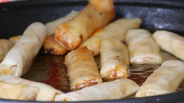 Asian spring rolls are fried in oil in a pan and turned over with kitchen tongs.