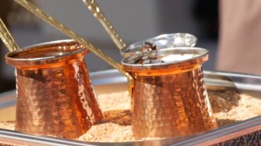 Turkish coffee in a copper pot on the sand. Delicious freshly brewed coffee is being prepared and boiled in a cafe on the street.