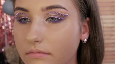 Profesyonel bir makyöz, genç ve güzel bir mankenin göz ve göz kapaklarına özel yapay elmaslar takar. Parlak moda yakın çekim görüntüsü.