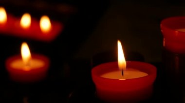 One flaming candle against a row of lit burning red round candles in a cathedral. Religious candles for the rest of the soul in the catholic church.