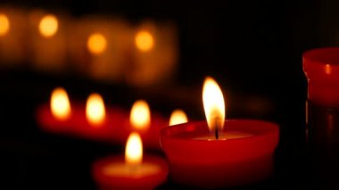 One flaming candle against a row of lit burning red round candles in a cathedral. Religious candles for the rest of the soul in the catholic church.