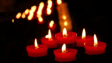 Several flaming candle against a row of lit burning red round candles in a cathedral. Religious candles for the rest of the soul in the catholic church close up view.