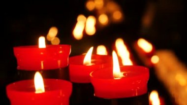 Several flaming candle against a row of lit burning red round candles in a cathedral. Religious candles for the rest of the soul in the catholic church close up view.