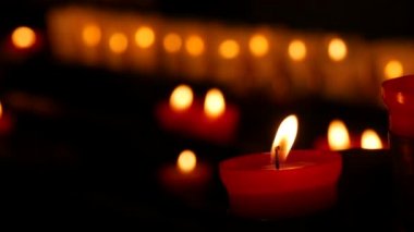 One flaming candle against a row of lit burning red round candles in a cathedral. Religious candles for the rest of the soul in the catholic church.