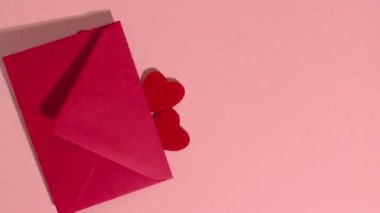Stop motion animation. Red hearts and wooden letters fall out of a red paper envelope that spell the word love on a pink background.