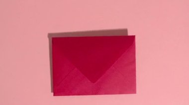 Stop motion animation. Red hearts and wooden letters fall out of a red paper envelope that spell the word love on a pink background.