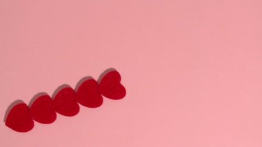 Stop motion animation. Red hearts and wooden letters that spell the word love on a pink background.