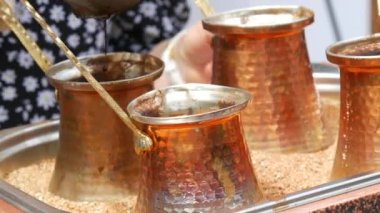 Ready freshly brewed turkish coffee in a turk on the sand, four copper turks close up view.