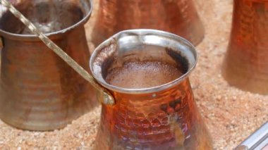 Ready freshly brewed turkish coffee in a turk on the sand, four copper turks close up view.